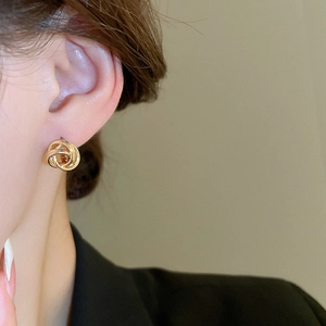 Close-up of golden braided geometric hoop earrings worn by a model in warm lighting