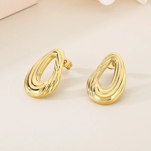 Détail macro de boucles d'oreilles en acier doré avec un design torsadé en goutte d'eau