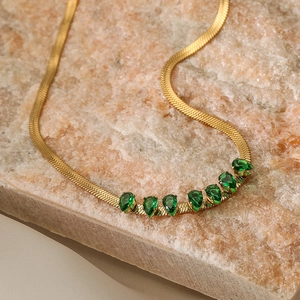 Golden snake chain necklace with seven emerald green teardrop gemstones on a stone plate
