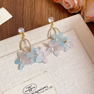 Detail of floral pendant earrings with zircons and pastel matte petals on beige surface