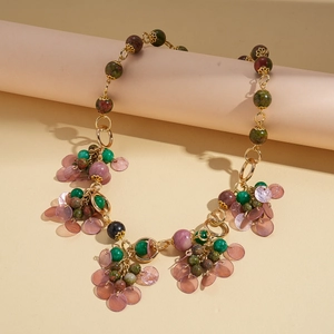 Detail of bohemian necklace with green stone beads and purple shell charms on gold chain