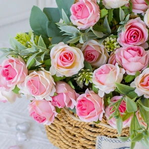 Pink and cream silk roses in a woven basket with green leaves and small buds detail