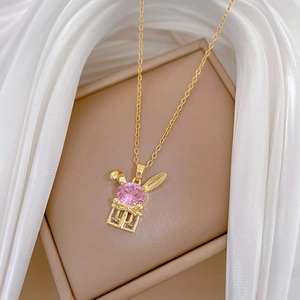 Detail of gold rabbit pendant with pink gemstone on silk fabric in jewelry box