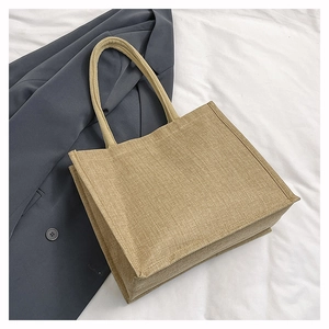 Detailed view of the woven linen texture and cylindrical handles on a beige tote bag
