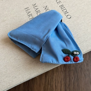 Close-up of light blue knitted hair tie with cherry embroidery and white pearls on a book