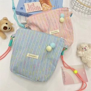 Detailed texture of tweed crossbody bags featuring colorful plush pom-poms and rope straps