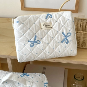 Detail of white quilted toiletry bag with blue polka dots and bow patterns on a wooden shelf