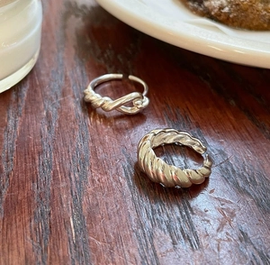 Detail of a 925 sterling silver knotted ring and ribbed ring on a dark wooden table