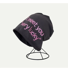 Dettaglio del testo ricamato in rosa I meet you su un berretto grigio scuro a maglia