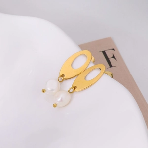 Elegant gold oval textured earrings with hanging white pearls on white ceramic