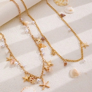 Detail of bohemian gold chain necklace with starfish, seashell, and pearl charms on sand