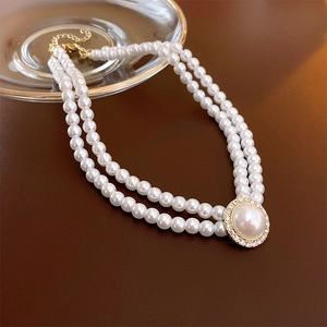 Gros plan du collier double rang avec perles blanches et pendentif doré serti de strass
