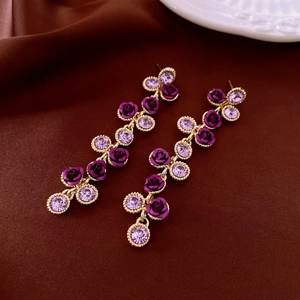 Dettaglio di orecchini vintage dorati con rose in vetro viola e cristalli lucidi