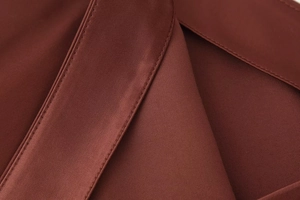 Macro detail of high-quality dark red satin fabric with smooth texture and fine stitching