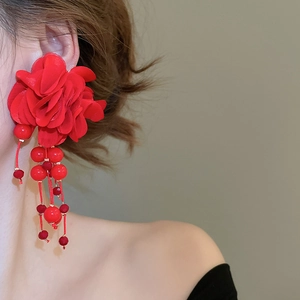 Detail of red fabric flower earrings with matching beaded tassels on a female model
