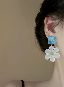 Detailed view of elegant blue and white acrylic flower drop earrings worn by a model