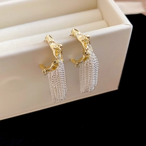 Detail of C-shaped gold textured stud earrings with elegant silver chain tassels