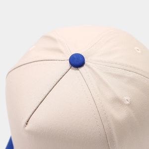Detail view of beige baseball cap top with royal blue button and reinforced stitching