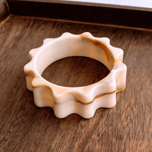 Détail d'un large bracelet en acrylique avec bords ondulés et texture écaille de tortue