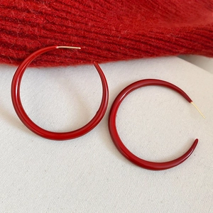 Detailed close-up of red enamel C-shaped hoop earrings with gold-plated silver needles