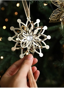 Detail of golden snowflake ornament with tassel and rhinestones held against holiday lights