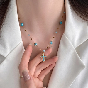 Close-up of golden necklace with blue stone beads and cross pendant on model