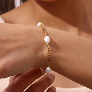Detailed view of a gold Cuban link bracelet with three baroque pearls on a wrist
