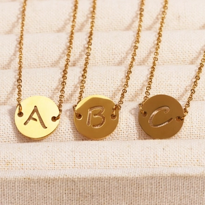 Détail de trois colliers dorés en acier inoxydable avec pendentifs ronds gravés A, B et C