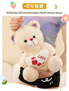 Close-up of beige plush teddy bear holding a white Love heart pillow with red nose detail