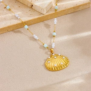 Gold shell pendant necklace with white pearls and blue beads on a sandy stone background