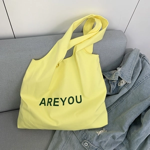 Detail of yellow canvas tote bag with AREYOU print resting on a modern grey sofa