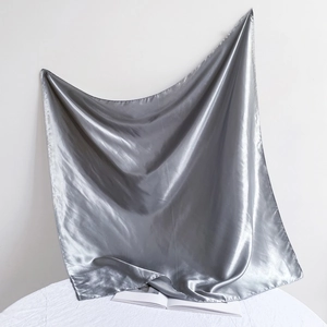 Artistic drape of a silver-grey satin silk square scarf on white textured surface