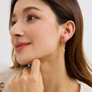Close-up of woman wearing golden starfish pendant earrings with a minimalist hoop design