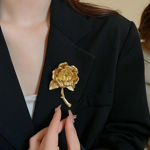 Detail view of a vintage gold rose brooch pinned on a black suit lapel with matte finish