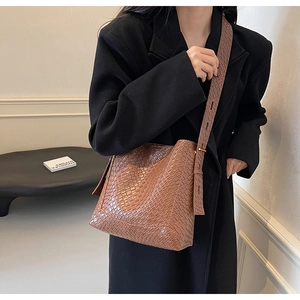 Detail of a brown woven texture bucket bag with matching wide shoulder strap on a model