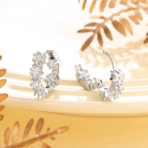 Star-shaped zircon silver earrings on ceramic plate with elegant golden leaf background