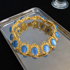 Detailed view of vintage gold hollow necklace with blue cat eye stones on metal tray