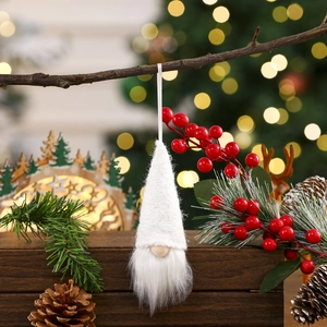 Close-up of a white knitted Christmas gnome hanging on a branch with bokeh lights background