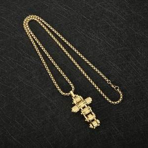 Flat lay of gold bicycle chain cross pendant on a black textured surface