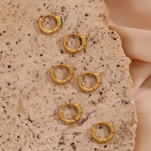 Détail de créoles dorées ornées de zircons verts, blancs et roses sur pierre