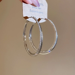 Detailed close-up of large intertwined silver hoop earrings with shimmering white zircon stones