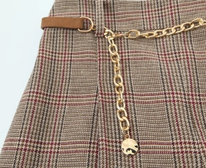 Detail of reddish-brown houndstooth skirt with golden metal chain and pendant belt
