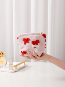 Pink plush cosmetics bag with red bow accent and floral zipper pull held in hand