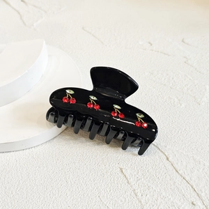 Detailed view of a black shark hair clip with red rhinestone cherry patterns on white texture