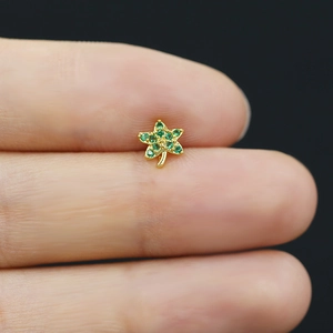 Close-up of gold maple leaf nose stud with green crystals held between fingers