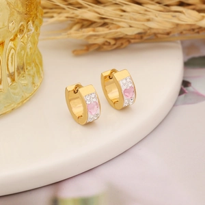 Macro view of gold-plated heart earrings with pink stones and zircons on white plate