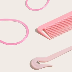 Pink hair braiding tool set with plastic comb and rubber bands on beige background