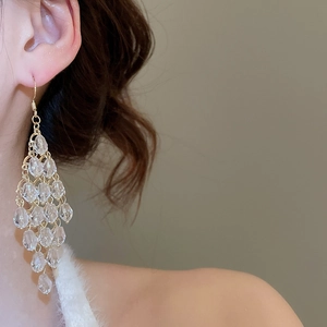 Close-up of long gold chain tassel earrings with clear faceted beads on a female model