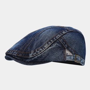 Detail of washed denim flat cap showing orange contrast stitching and metal adjustment buckle