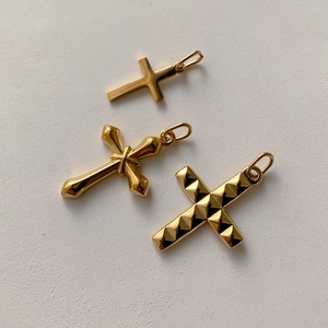 Tre ciondoli a croce e a X dorati in stile minimalista e gotico su uno sfondo bianco puro